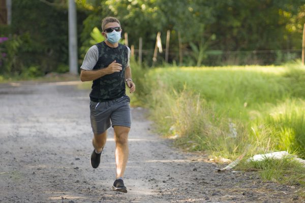 covid-19 deconfinement - young attractive and happy man outdoors in city park doing running workout wearing protective face mask jogging and training after long days of quarantine